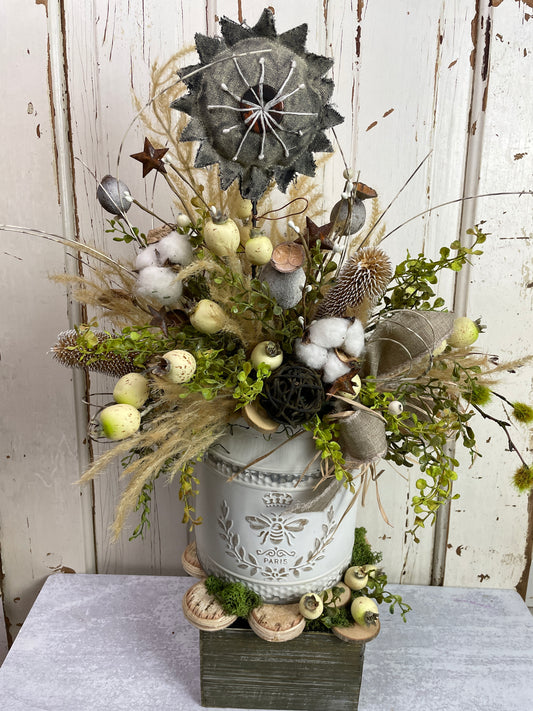 A primitive country style floral design for your table with a fabric flower and real cotton bolls in a vintage style metal bucket container
