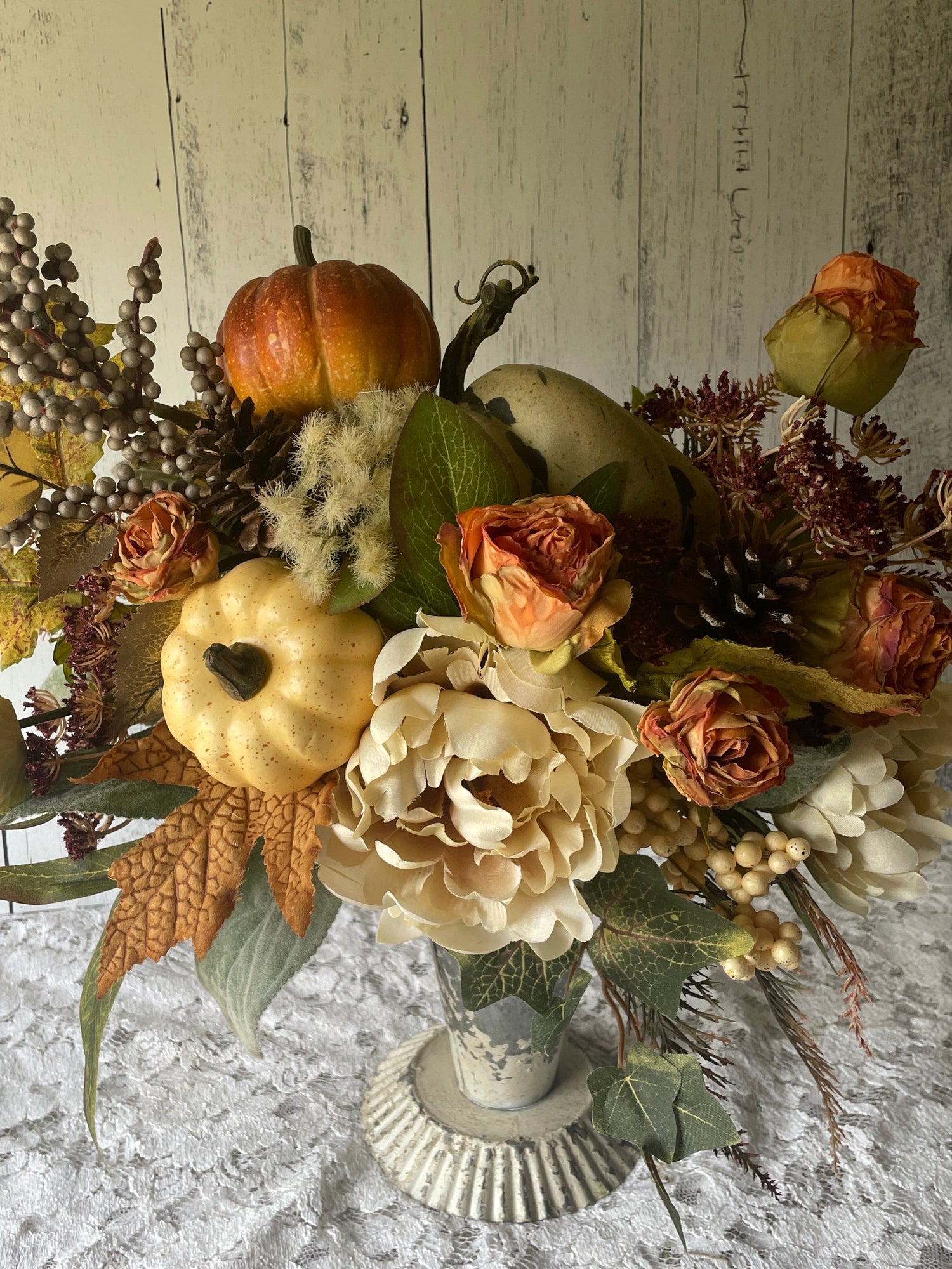 Autumn-themed floral arrangement with pumpkins and leaves on a textured surface.