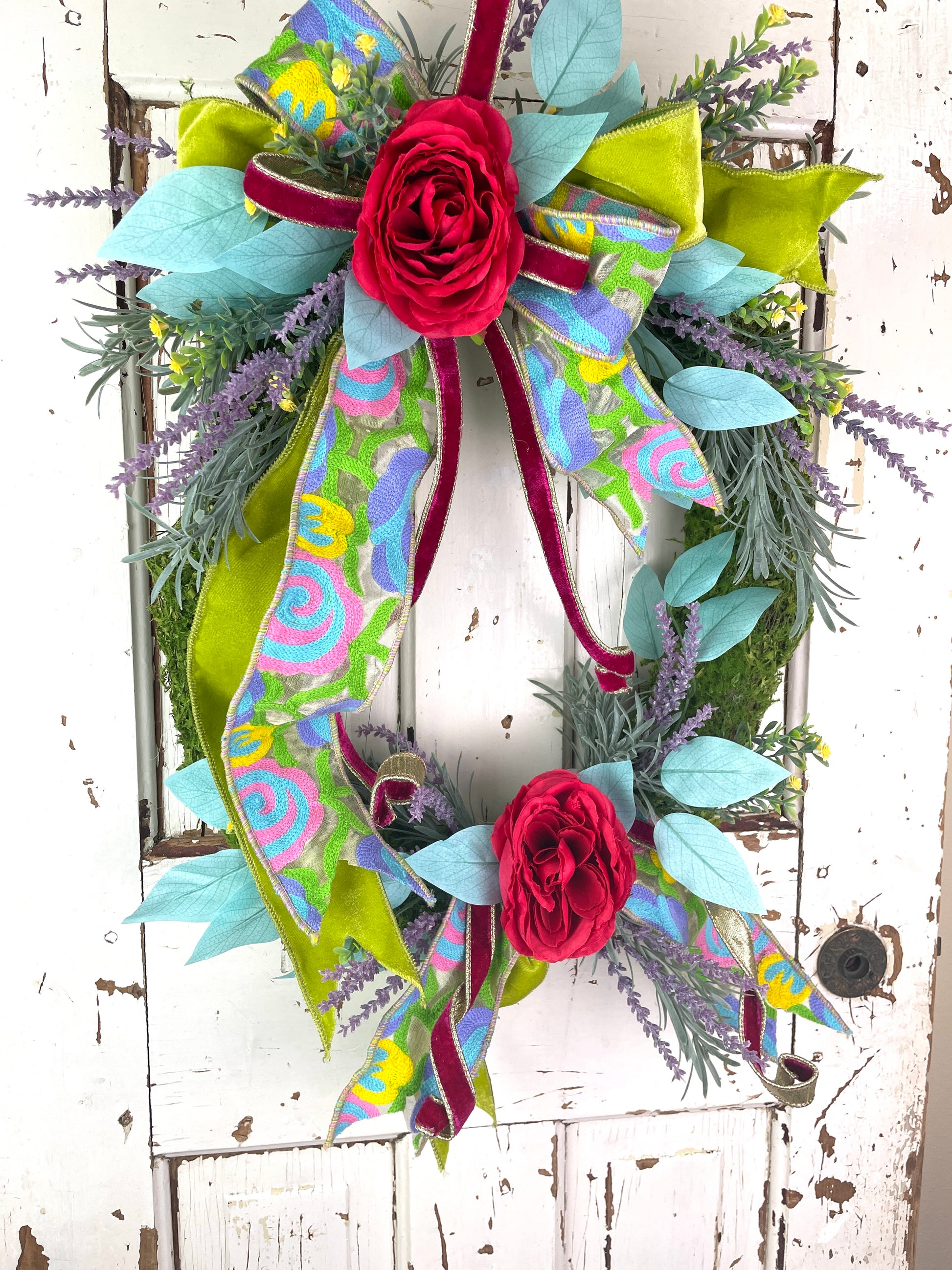 Large oval floral wreath with bright flowers and velvet ribbons that has roses and lavender