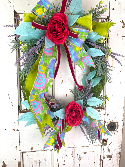 Large oval floral wreath with bright flowers and velvet ribbons that has roses and lavender
