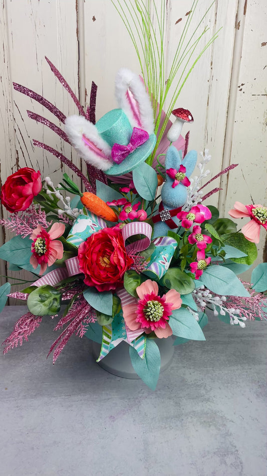 A whimsical Easter centerpiece with bright flowers and leaves, and featuring a bunny and top hat with bunny ears