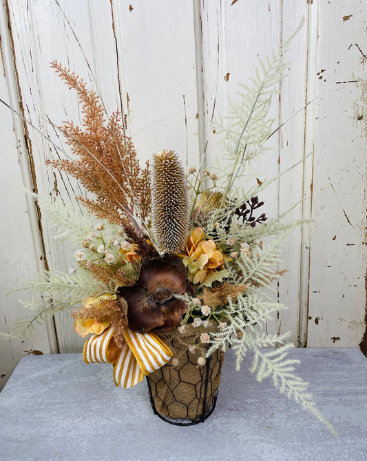 Boho style floral arrangement with dried pods and grasses in neutral colors in a wire basket with burlap 