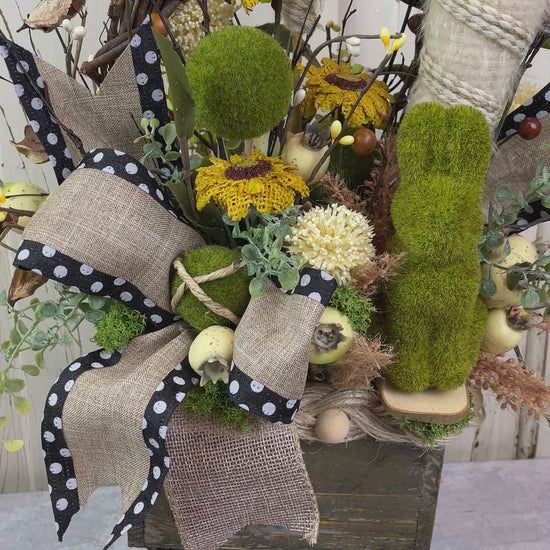A wooden box with a primitive style arrangement of fabric sunflowers and a moss bunny with burlap carrots 