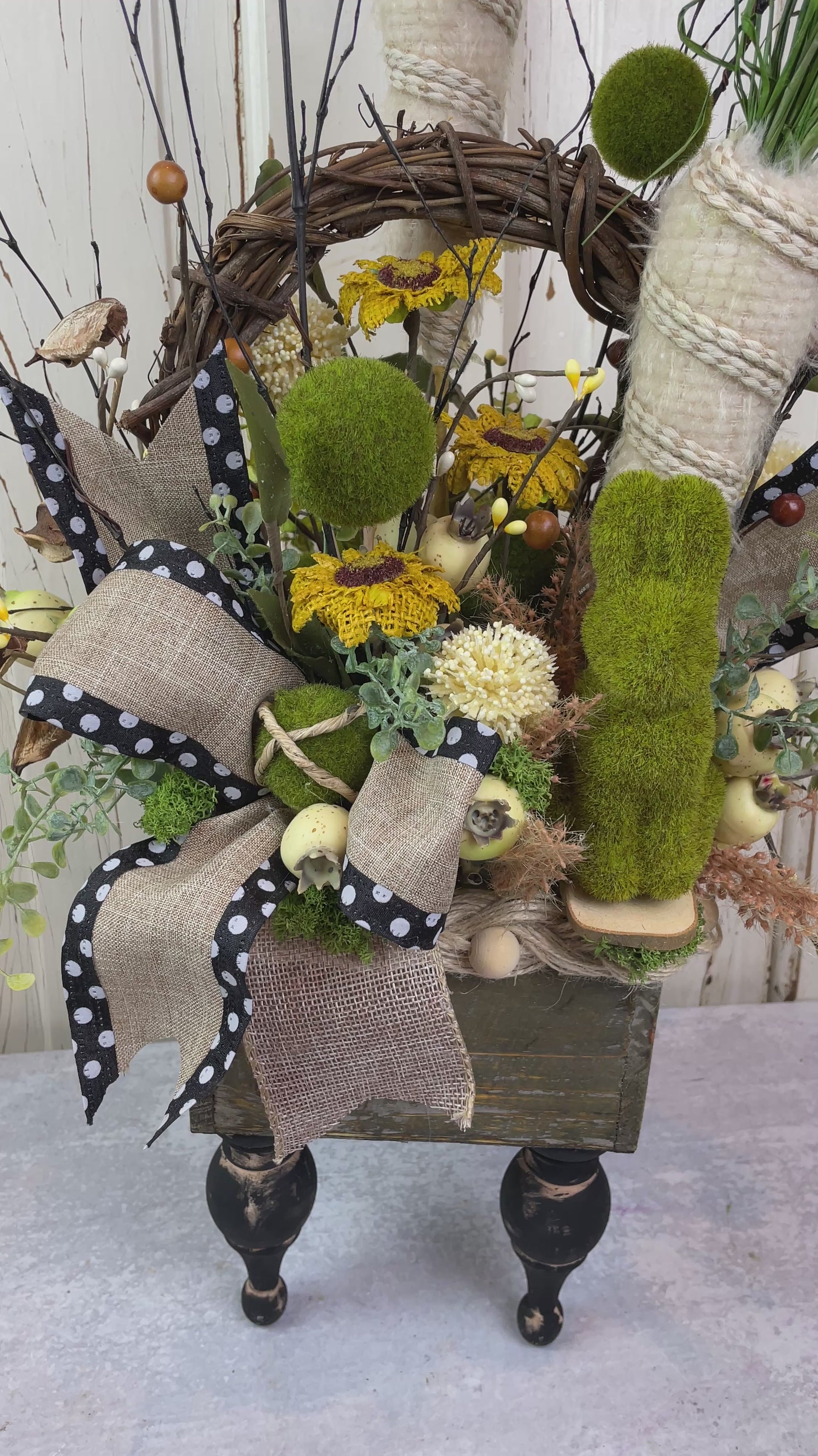 A wooden box with a primitive style arrangement of fabric sunflowers and a moss bunny with burlap carrots 